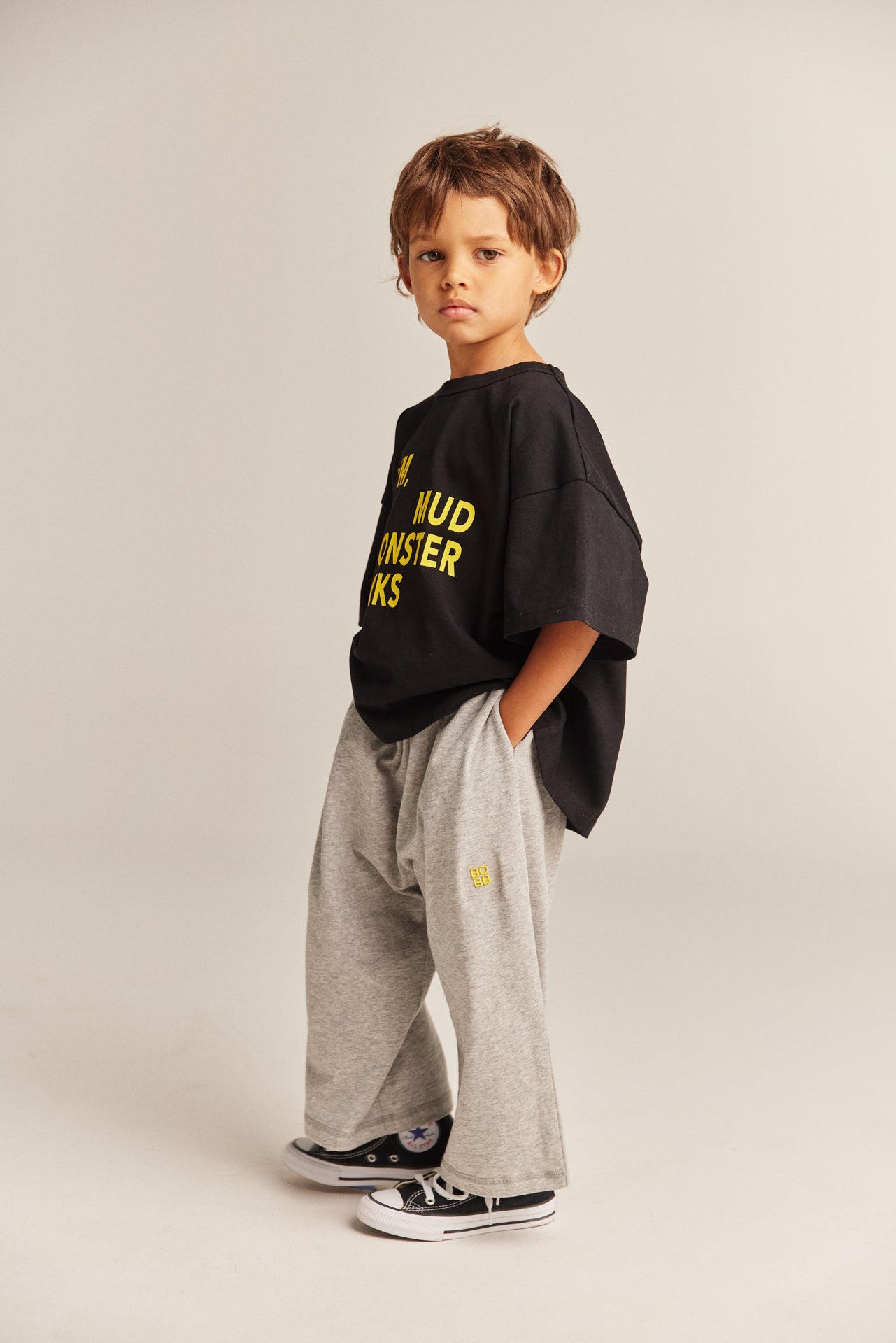 Child wearing a black oversized shirt with yellow text and gray pants on a plain background